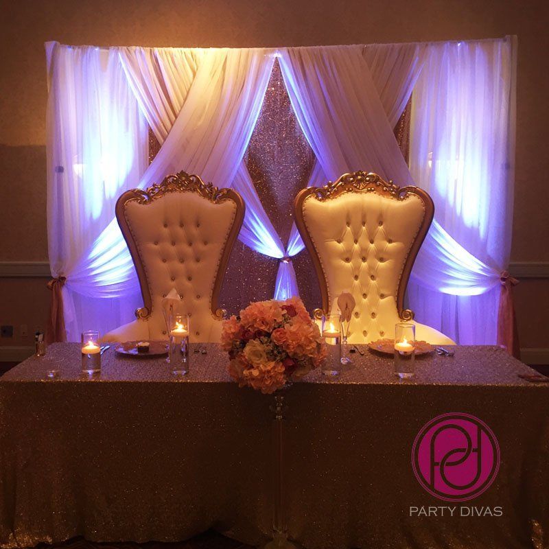 Head table event design with an elegant draped background, floral display, candles and thrones.