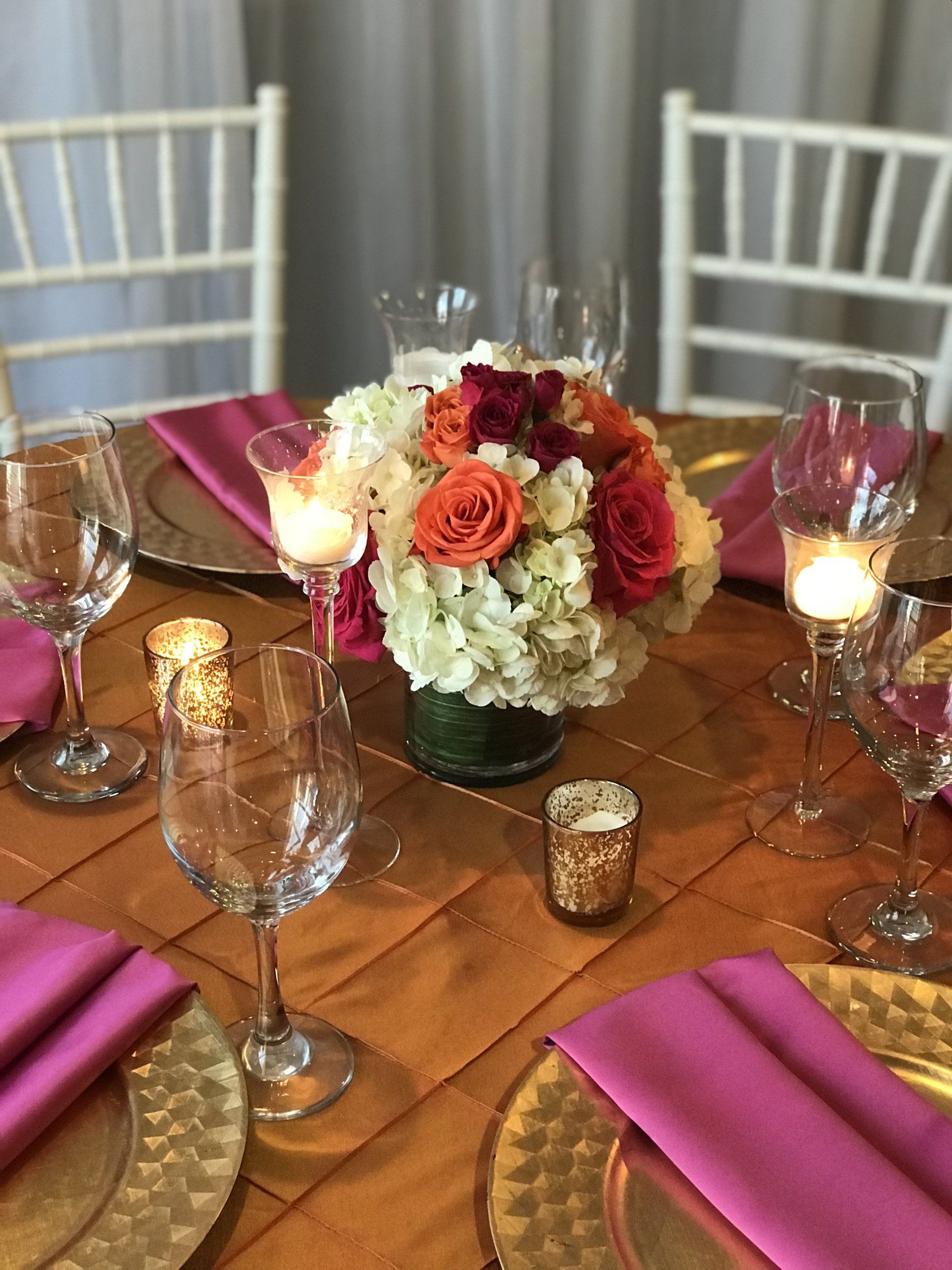 floral arrangement in a cylinder glass vase, candles, gold chargers, and napkins on table.