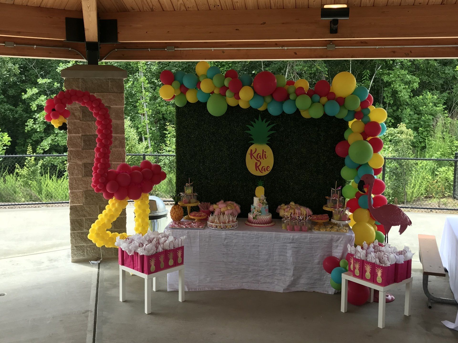 Kali Rae's party desert and favor tropical display with a grass wall background and multi color balloon garland.