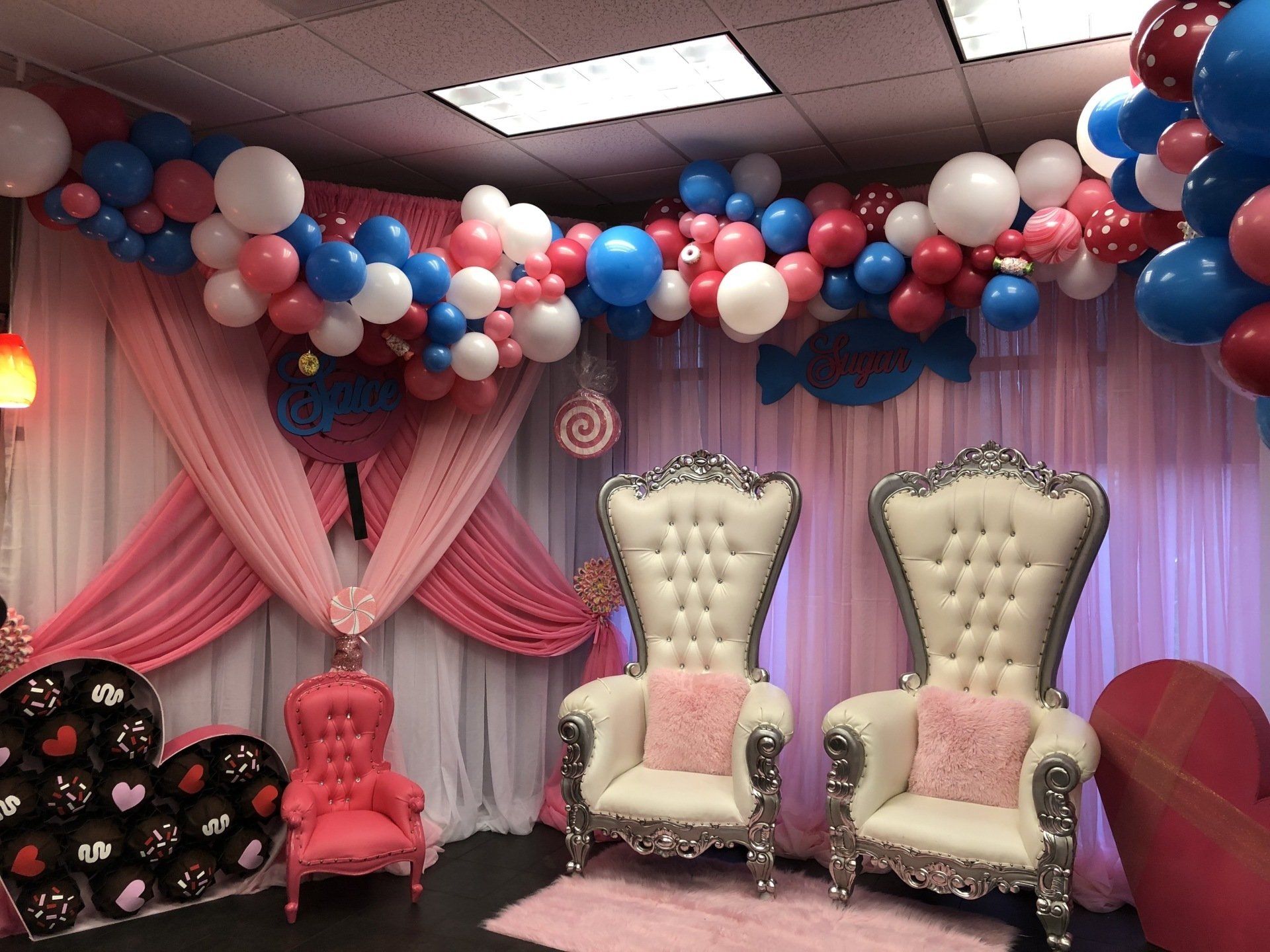 Red blue and white balloon ceiling installation with draped pink backdrop and throne chairs for kids party