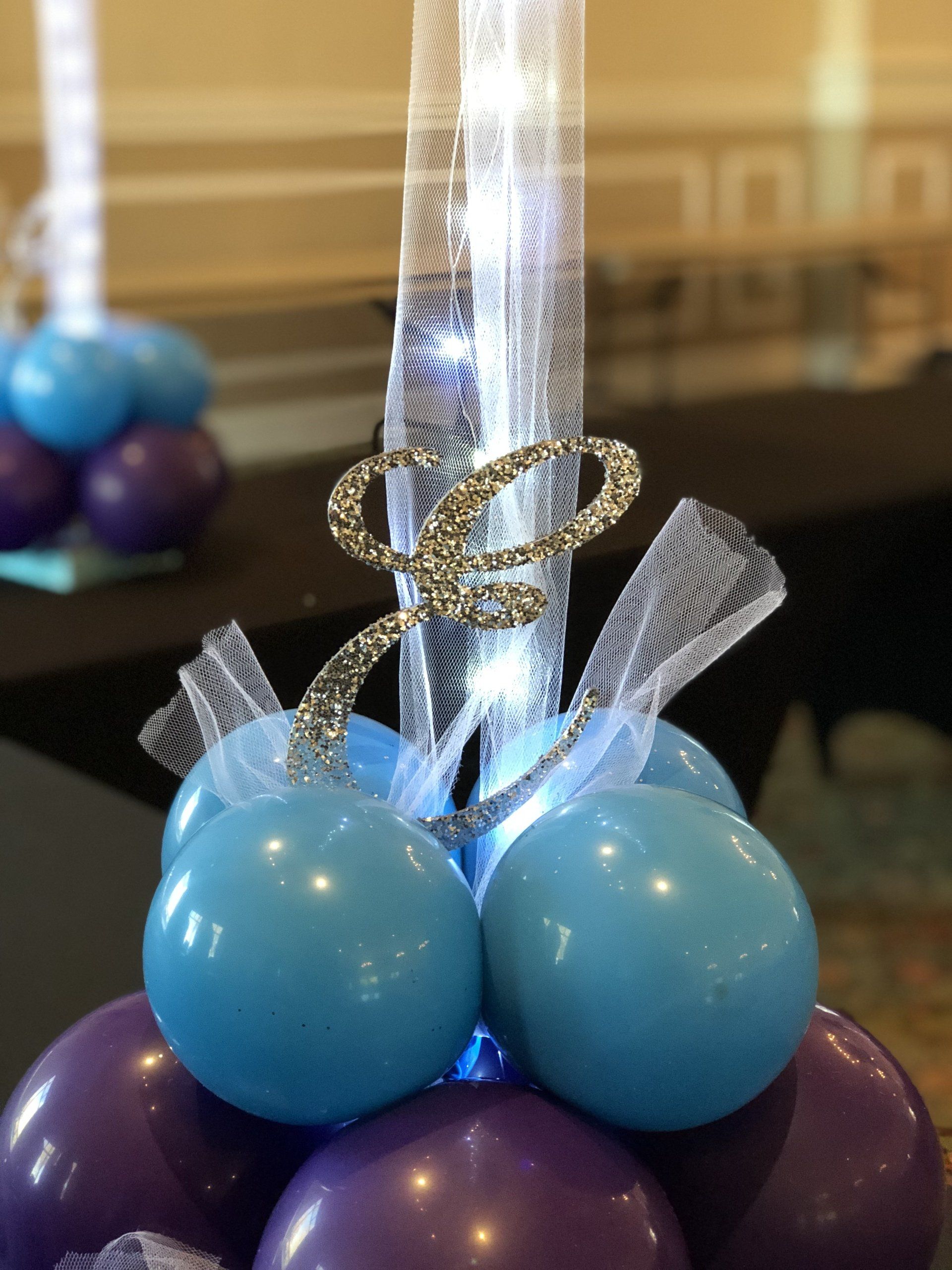 A centerpiece designed with balloons as the base, a sparkly cursive E and lace entwined with lights that extend above.