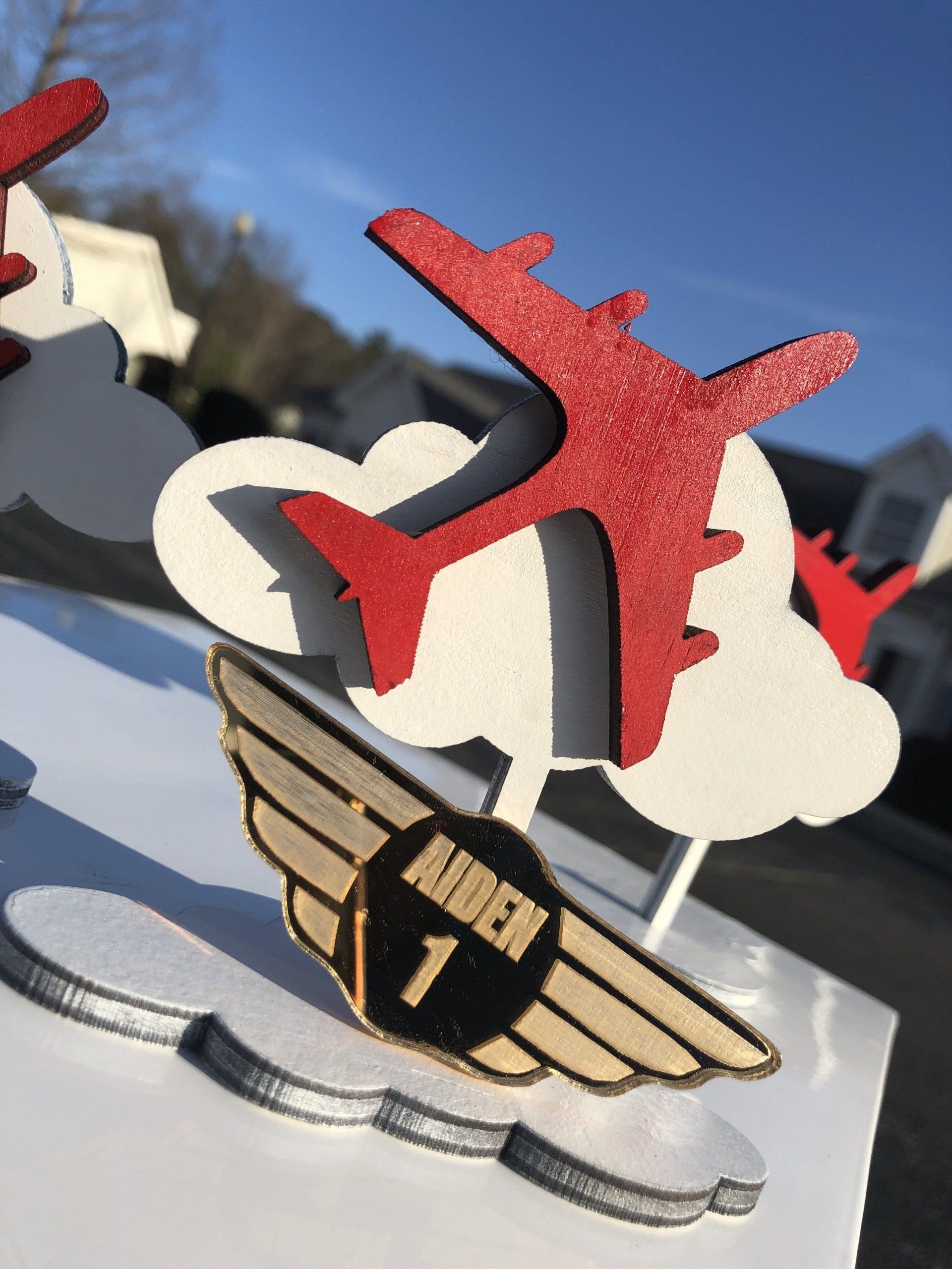 Multi layered and material laser cut airplane themed party accessory with a red plane flying out of white clouds.