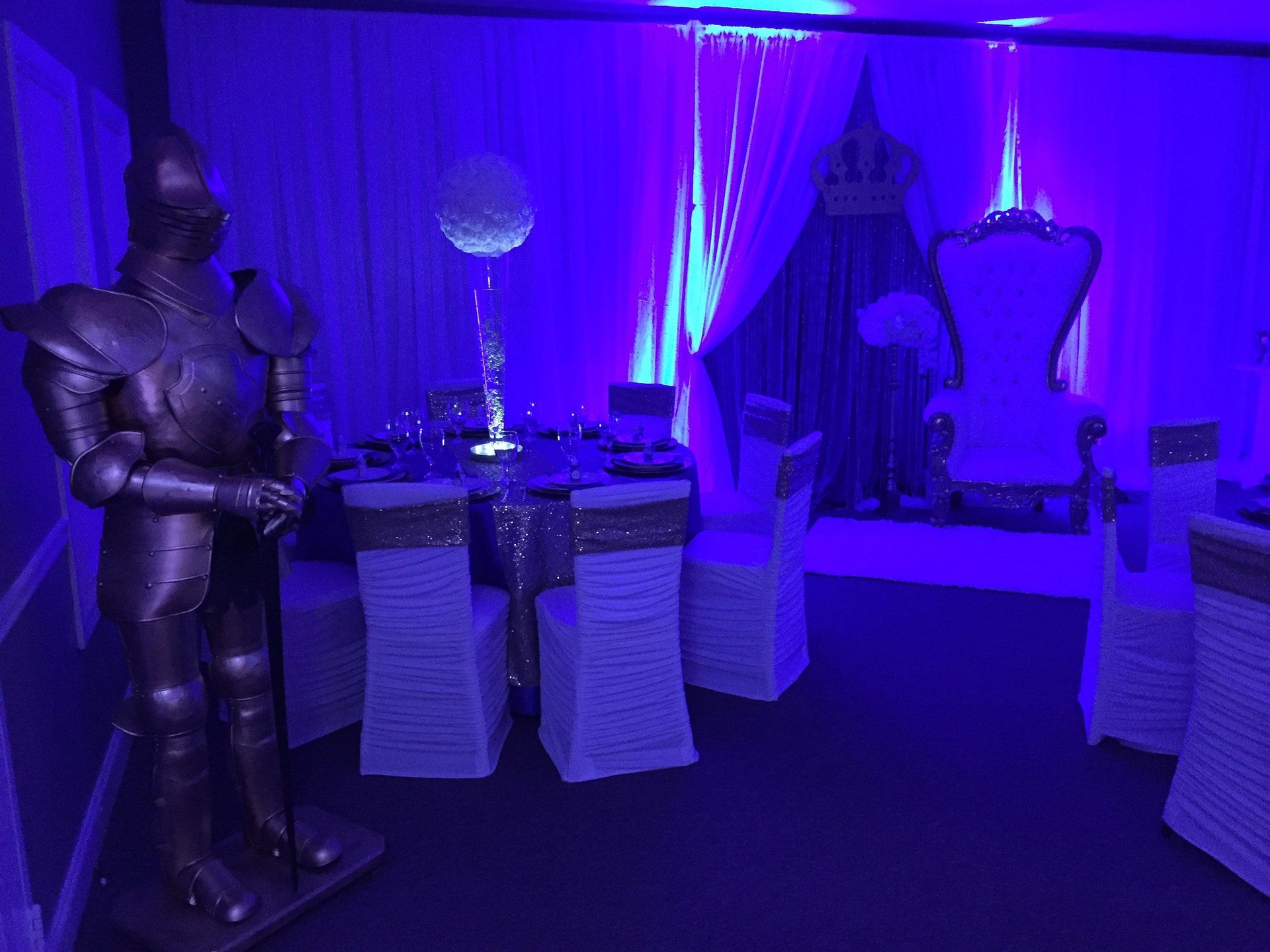 Royal themed event setup with throne chair purple uplighting and dramatic backdrop décor