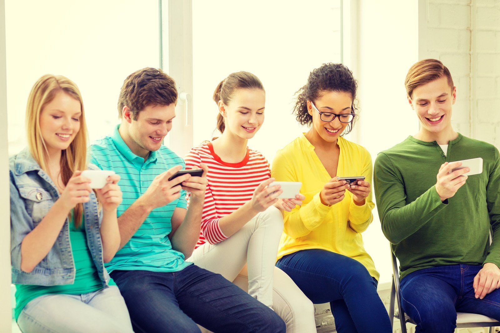 Group of young people sitting together looking at their phones.