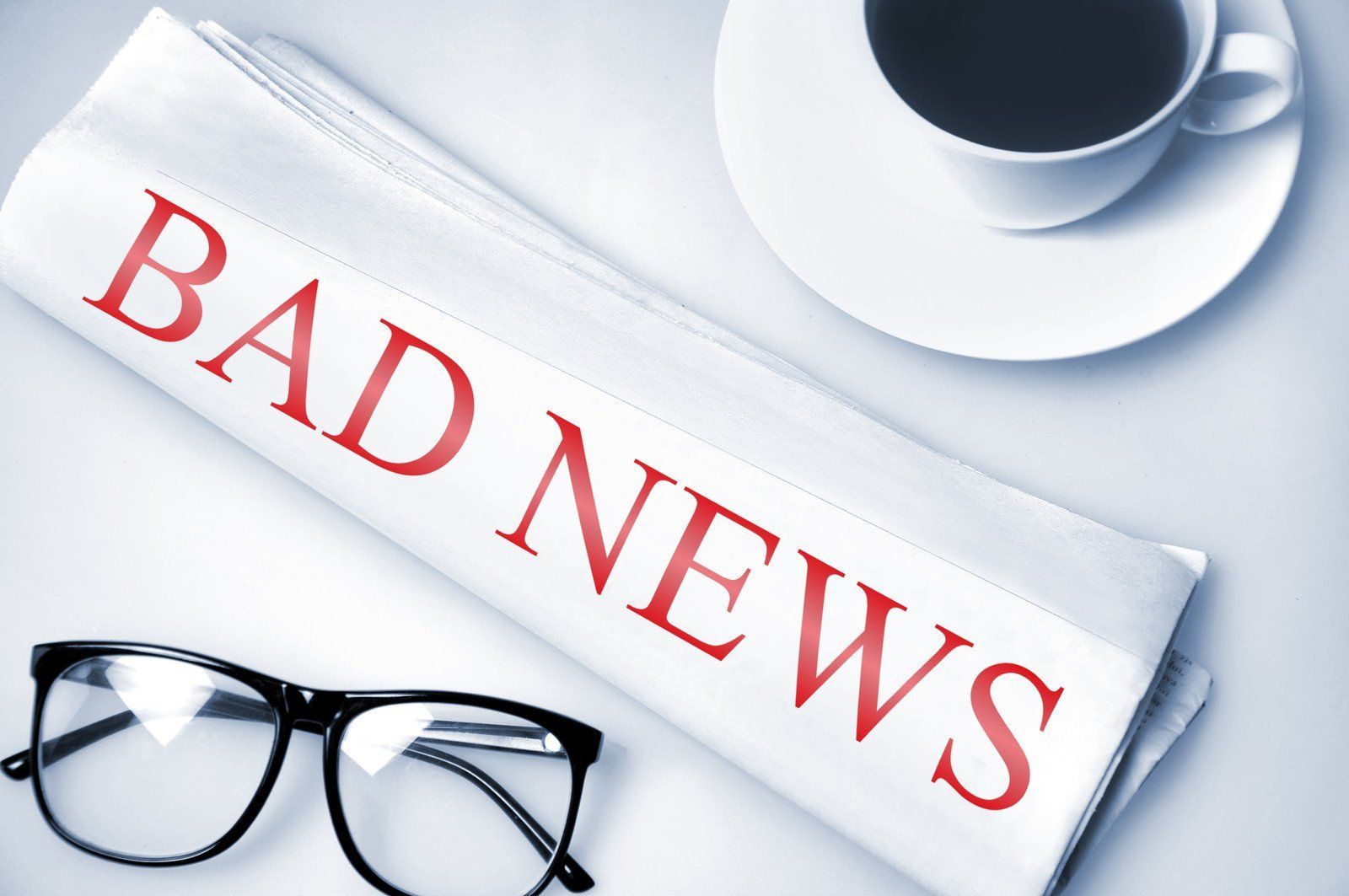Folded newspaper that says bad news next to reading glasses.