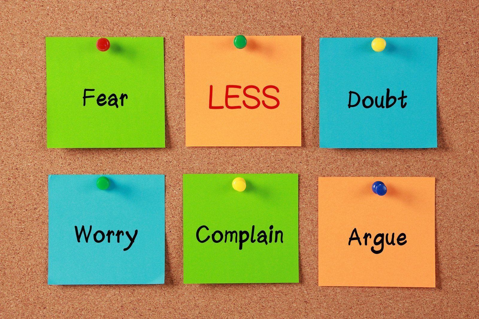 Six sticky notes pinned to a cork board with the words fear less doubt worry complain argue written on them.