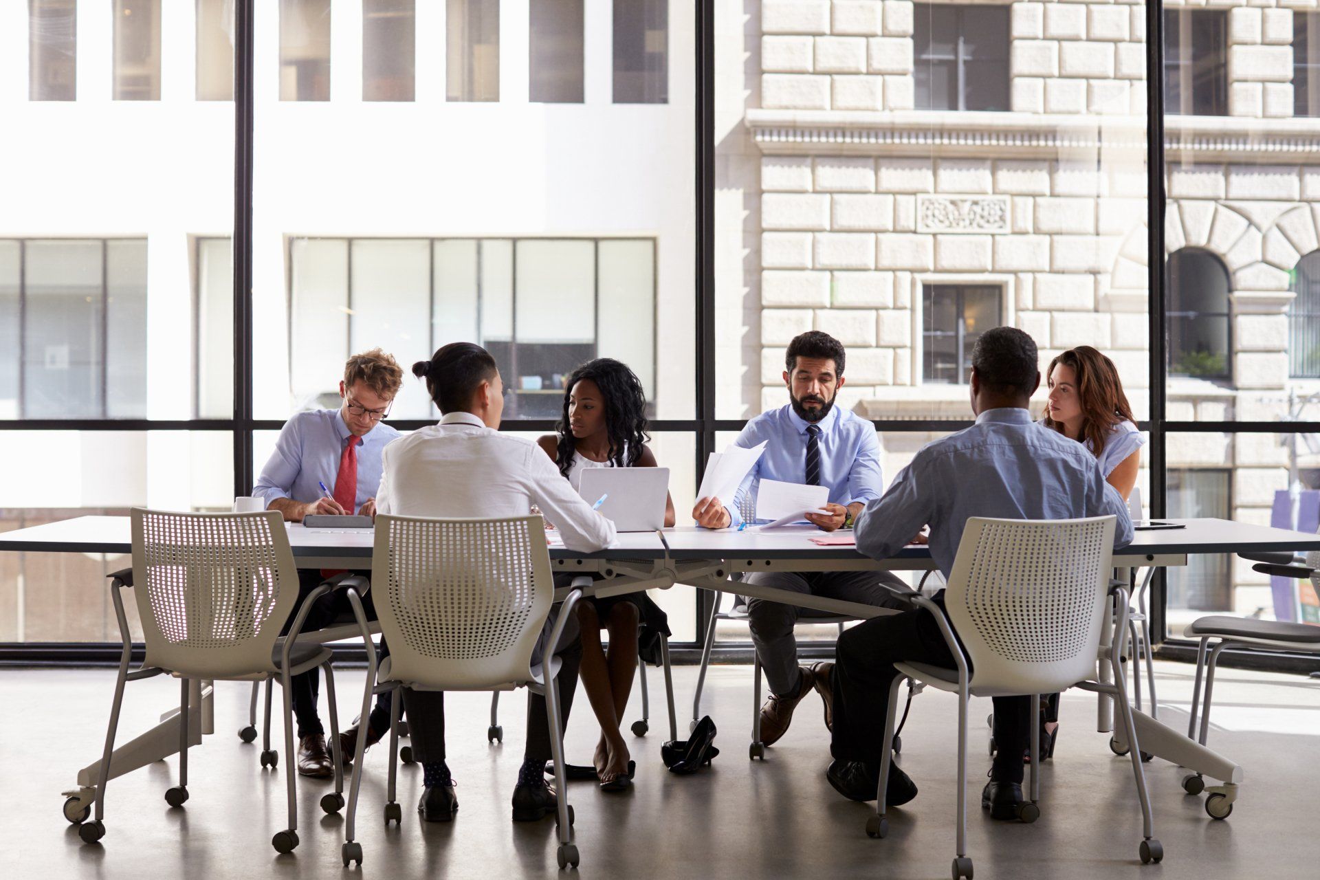A group of business people are sitting at a long table having a meeting.