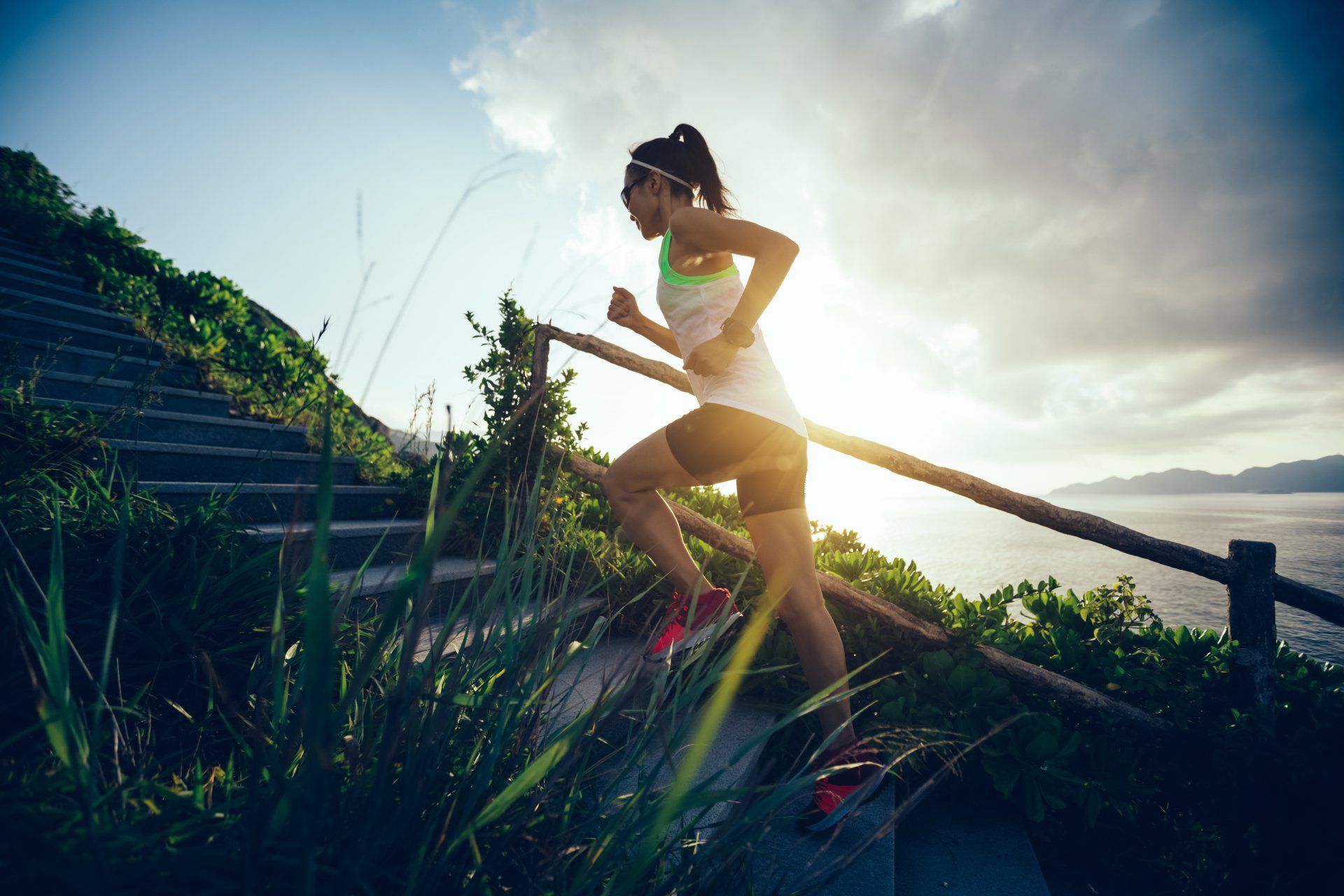 A woman is running up a set of stairs near the ocean.