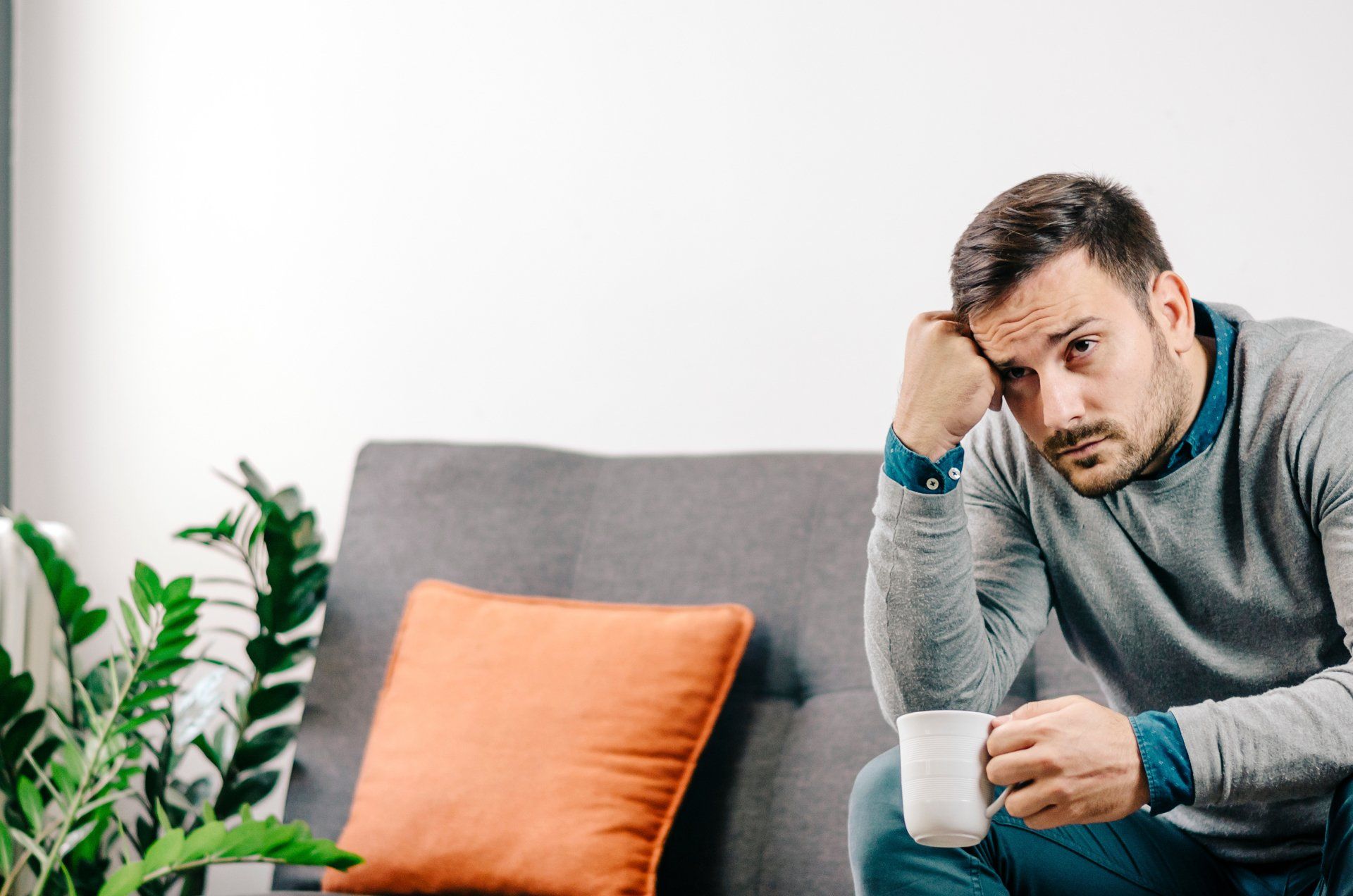 A man is sitting on a couch holding a cup of coffee.