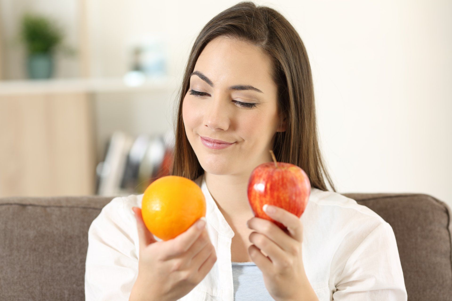 A woman is sitting on a couch holding an apple and an orange.