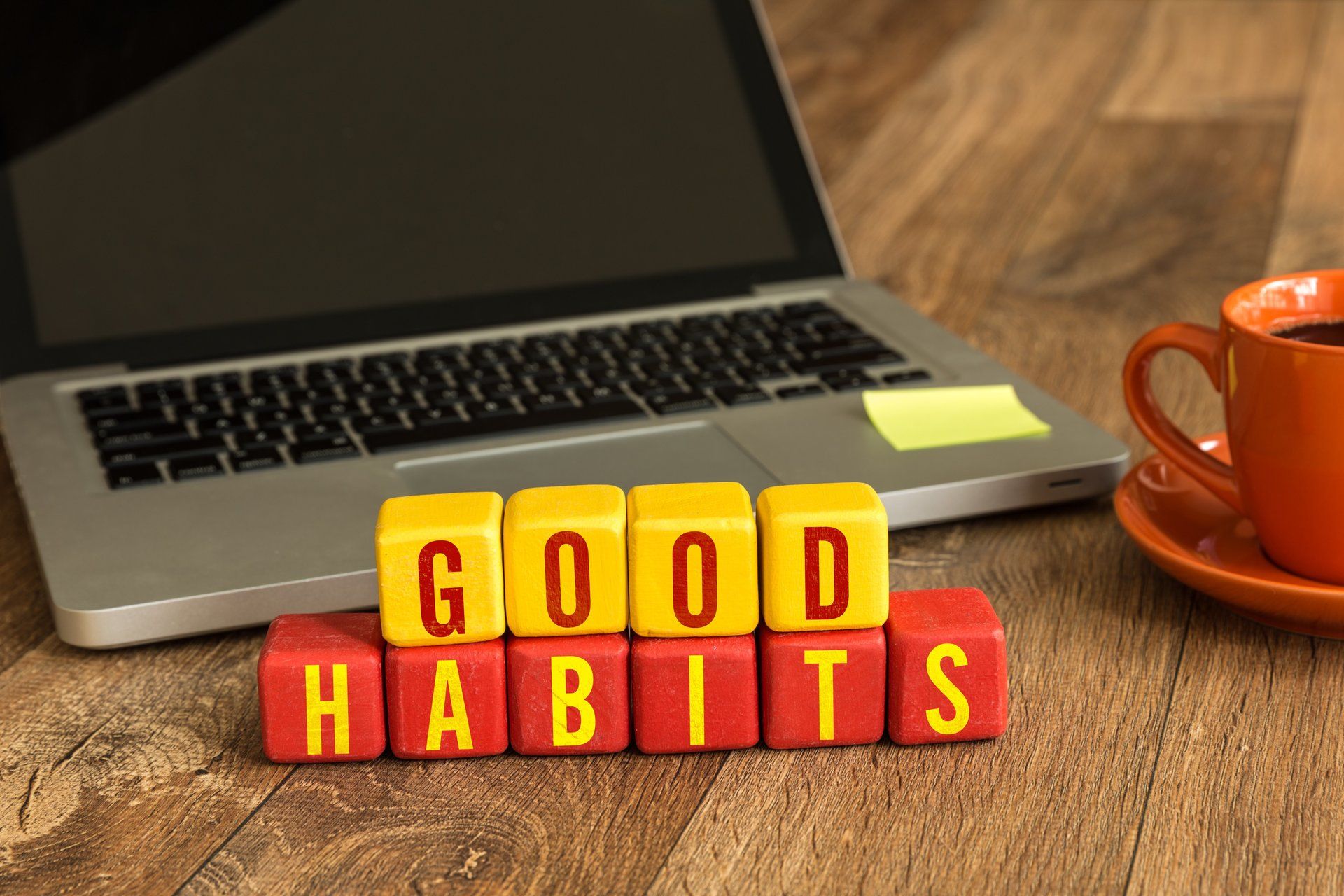 Laptop computer next to wooden blocks that spell out good habits.