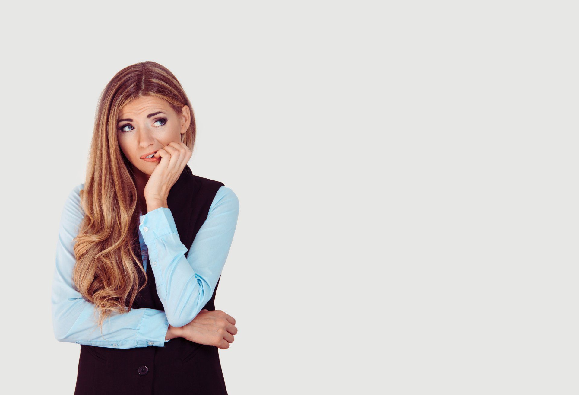 An anxious woman is standing with her arms crossed and her hand on her chin.