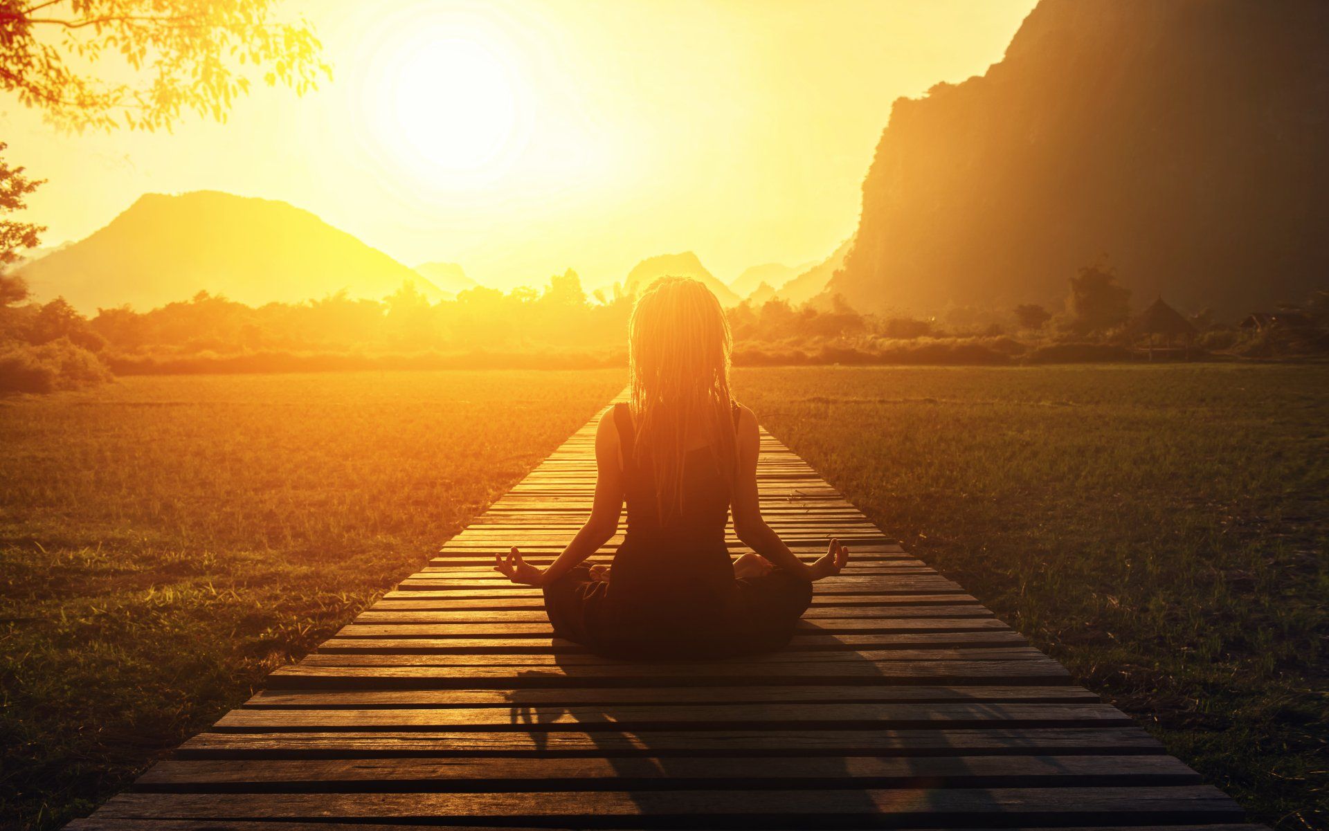 A woman is sitting in a lotus position on a wooden pier at sunset.