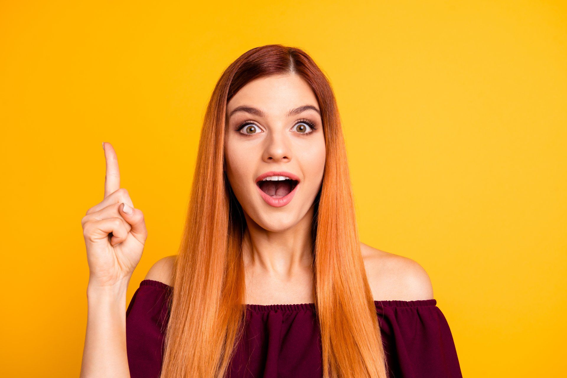 A woman with long red hair is pointing up with her finger.