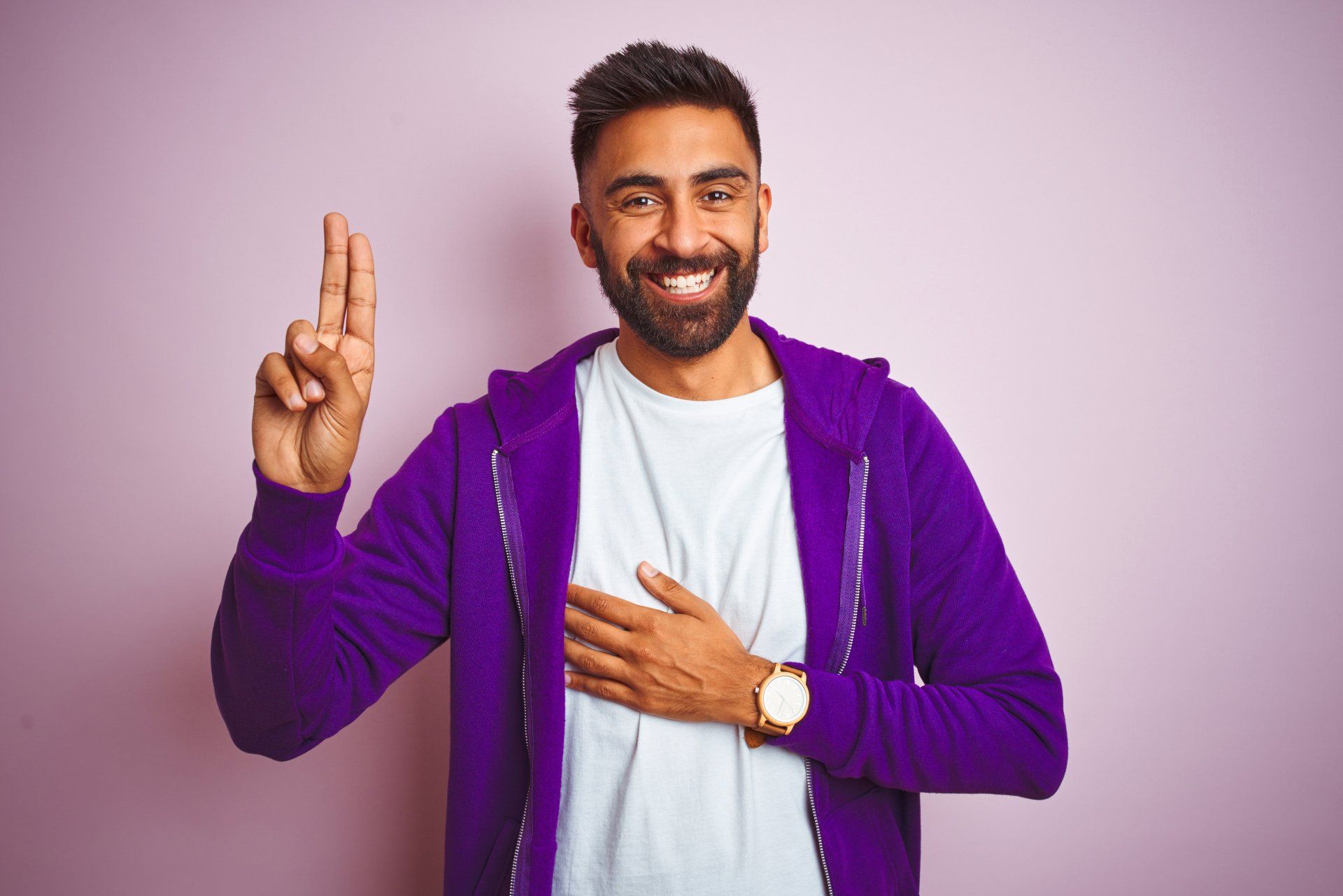A man in a purple jacket is smiling and making a peace sign with his fingers.
