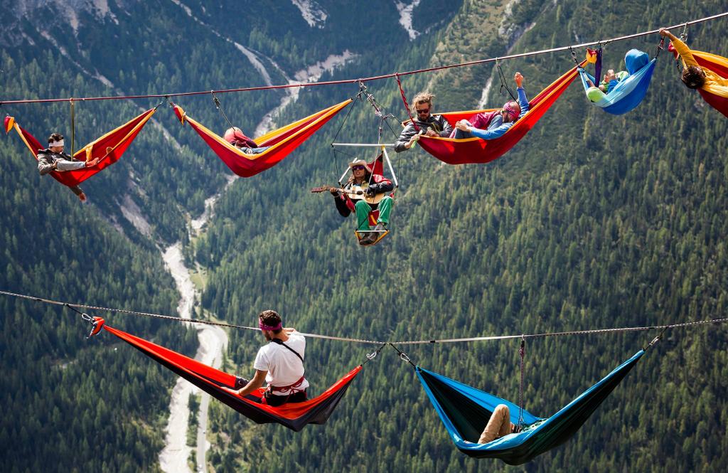A group of people are laying in hammocks on a rope in the mountains.