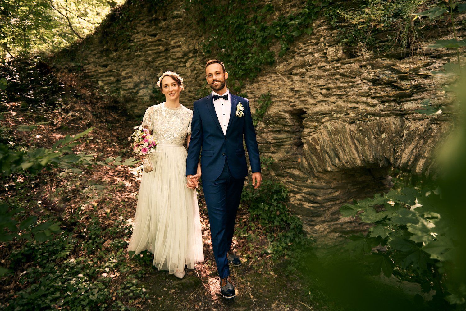 Paar,Hochzeit,Hochzeitspaar,Liebe,Händchen halten,Glücklich,Hessen,Ruine,Wald,jung,Strauß;Anzug,Kleid,Brautkleid,Braut,Bräutigam,Fliege,Blumen,Lächeln,Lederschuhe,Sonnenlciht,Sonne