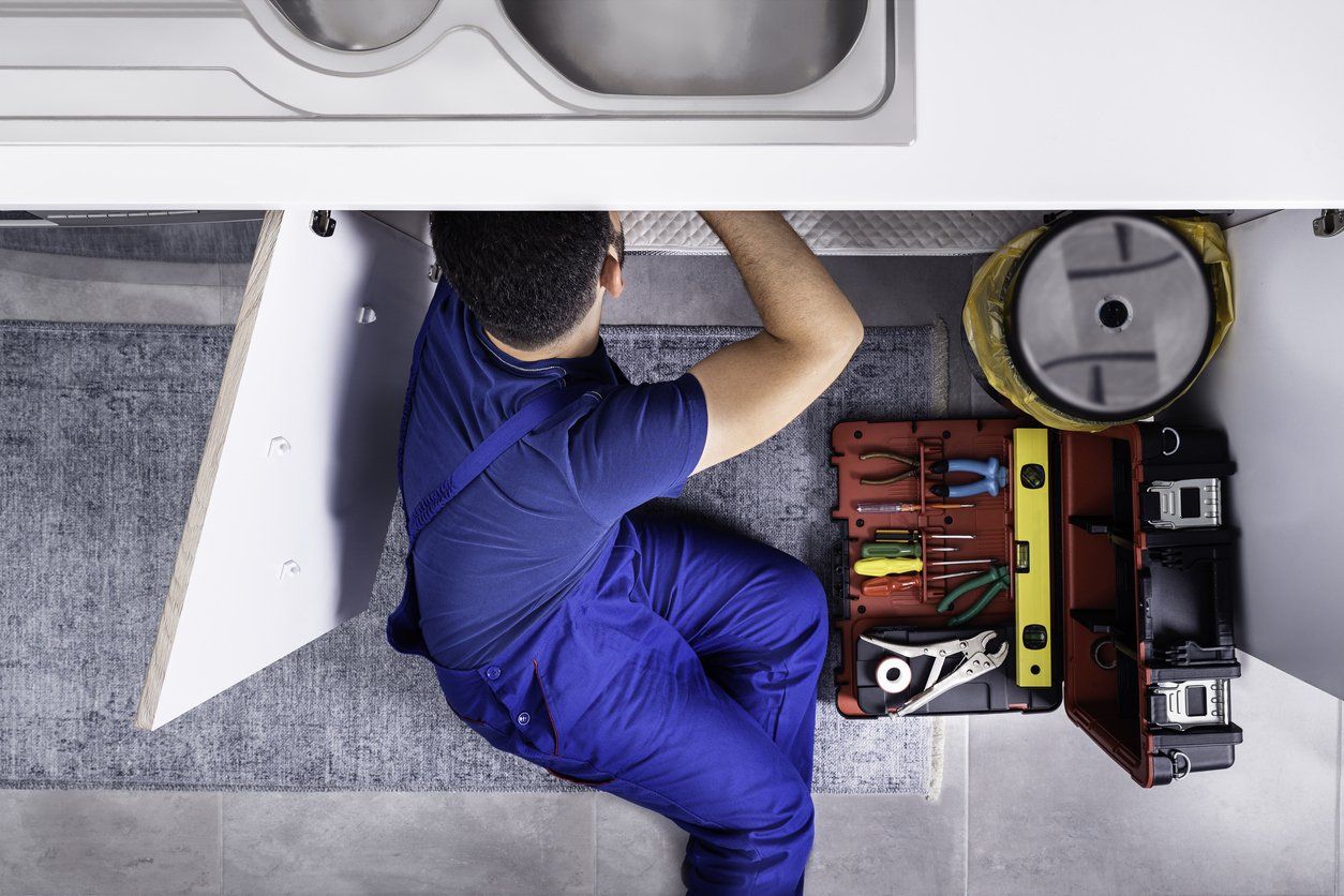Person in blue overalls working with tools in a small maintenance compartment.
