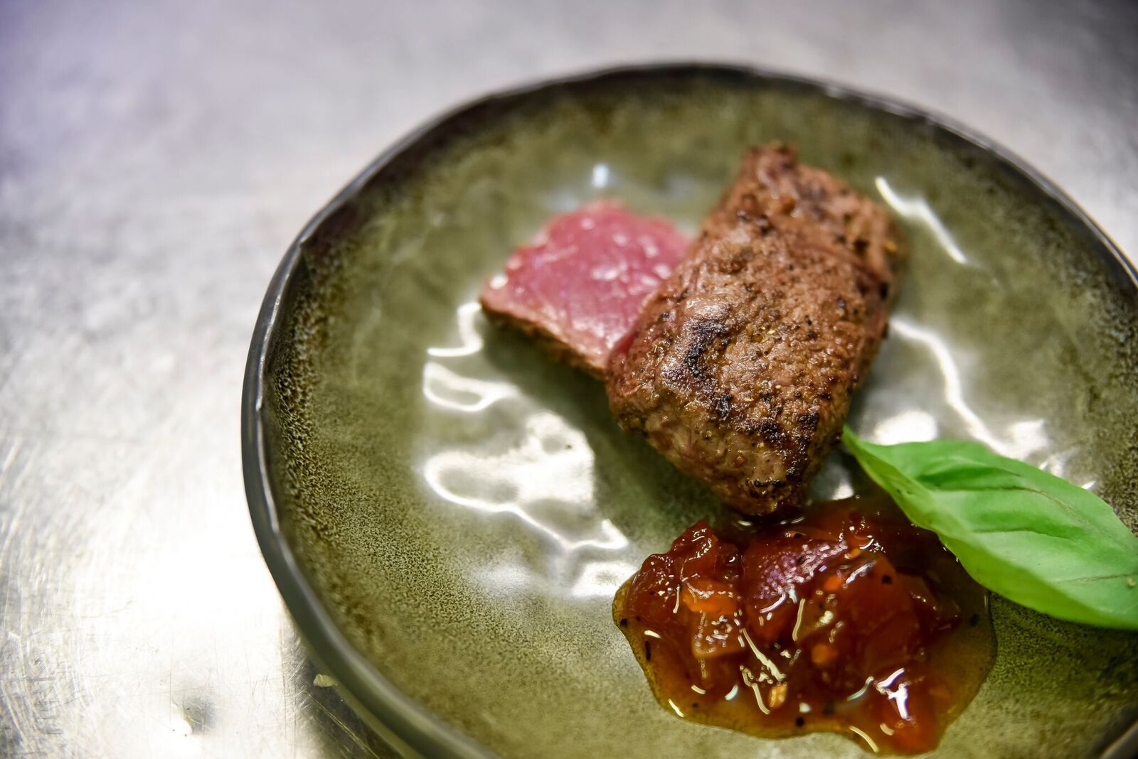 Green plate with sliced seared meat and glossy sauce, garnished with a basil leaf