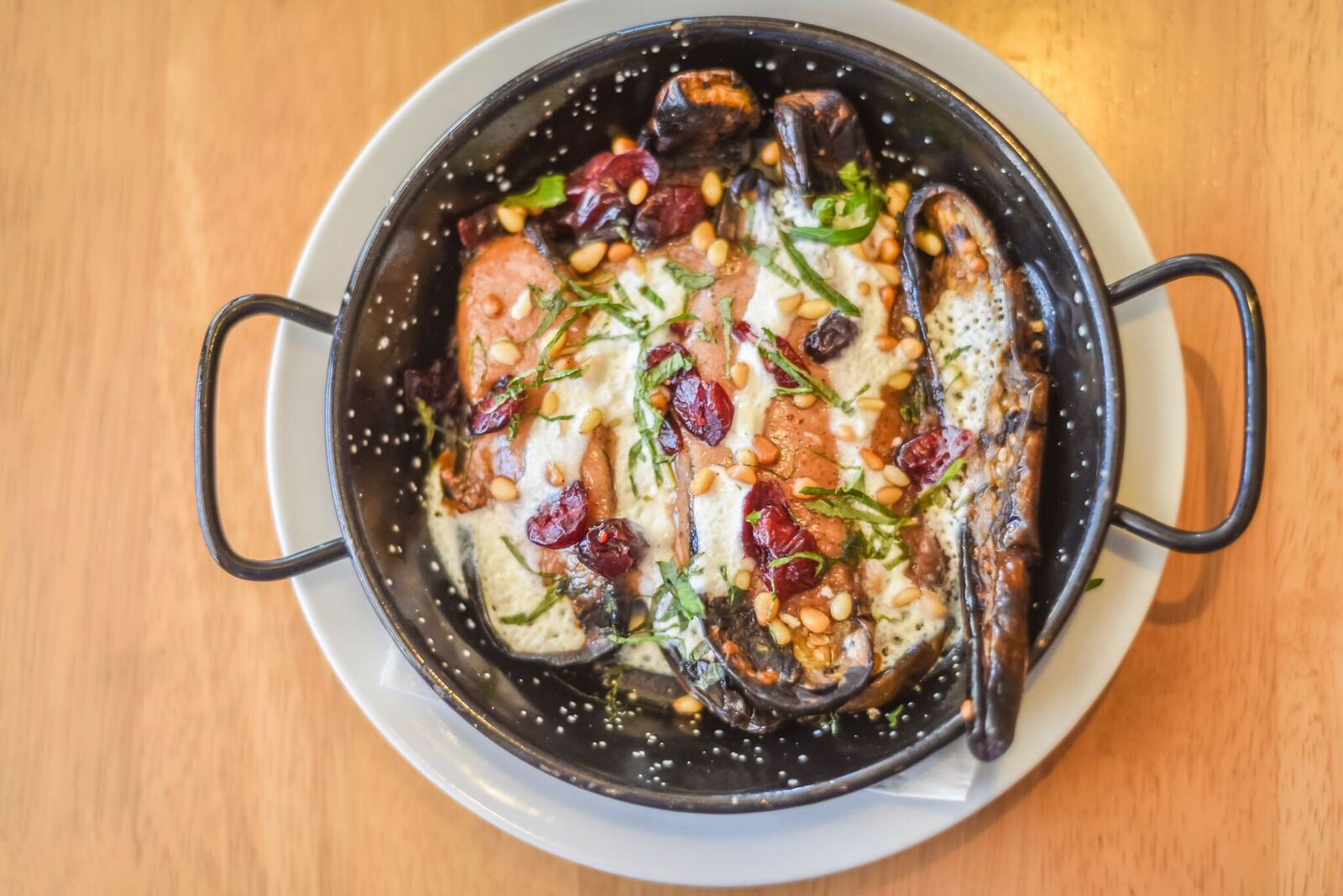 Two grilled fish fillets in a black pan with herbs and sauce on a wooden table