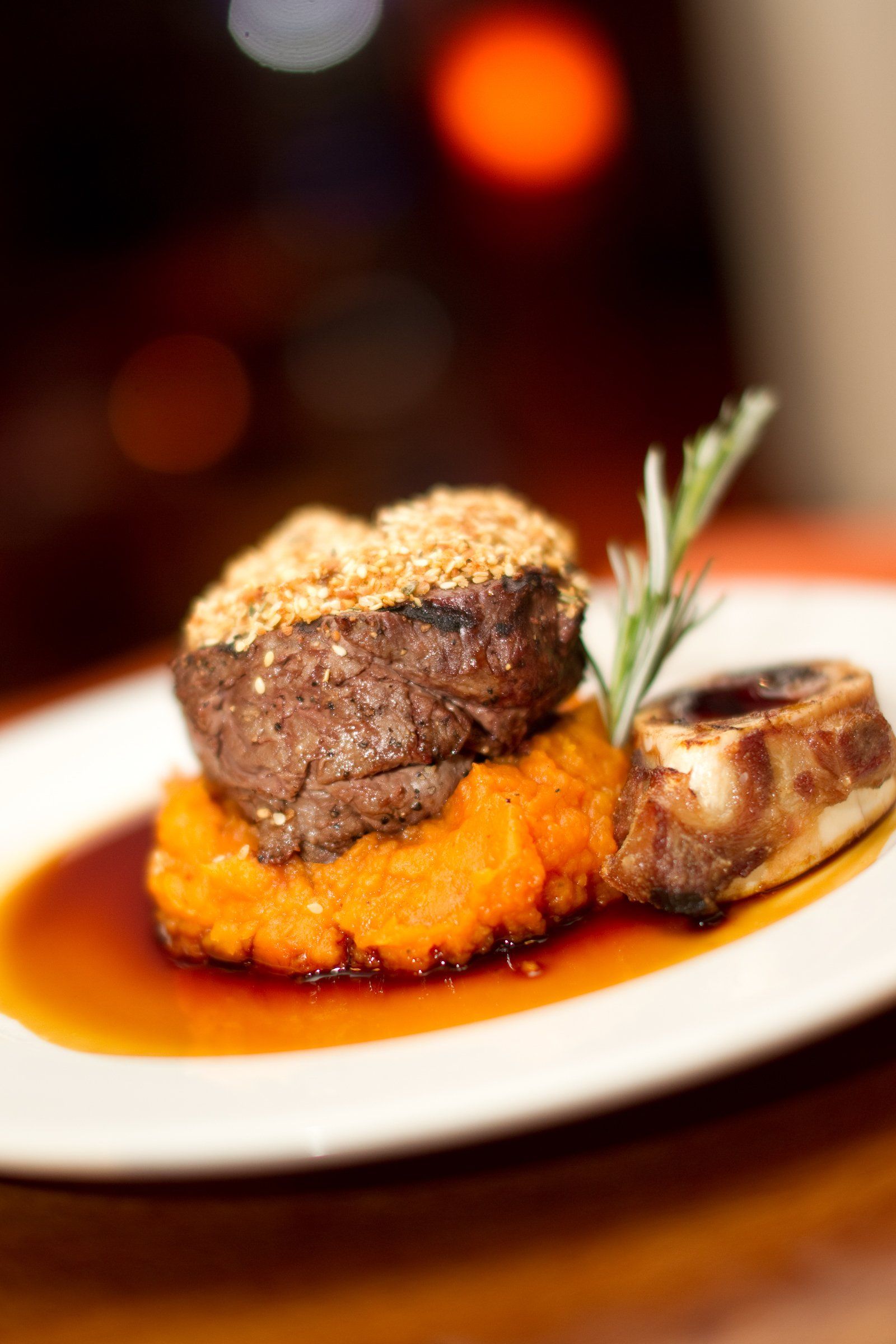 Plated gourmet steak over crispy hash browns with rosemary and sauce on a white plate