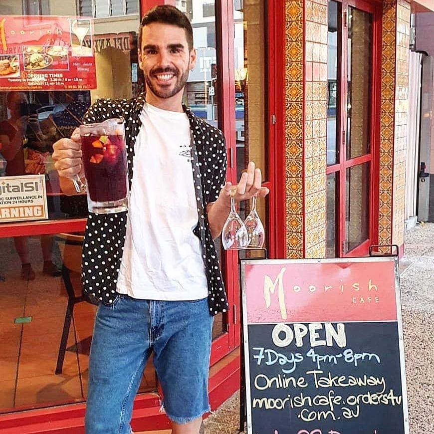 Man holding a drink and a bottle outside a café with an OPEN sign