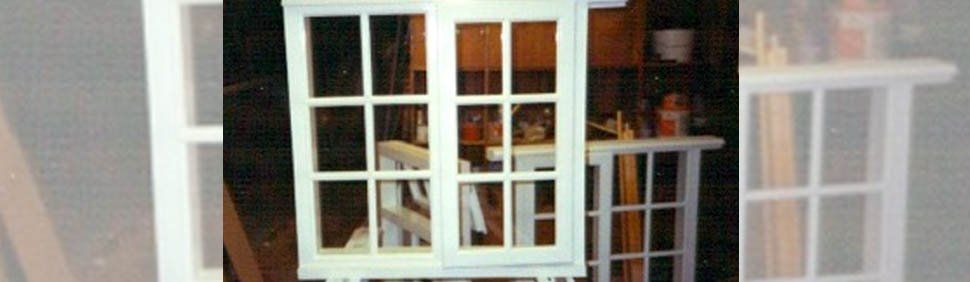 A white wooden window frame with glass panes standing in a cluttered workshop.