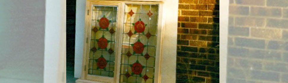 A window with red and green stained glass floral patterns, set against a dark brick wall.