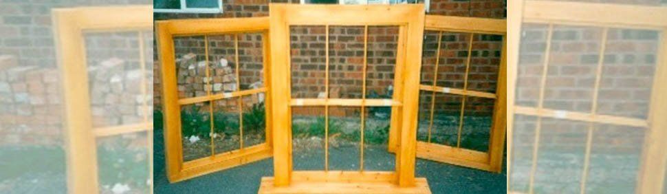 Four wooden window frames with grid-pattern muntins arranged in front of a brick building.