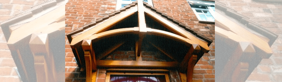 A wooden triangular porch canopy with a curved beam, attached above a doorway on a red brick house.