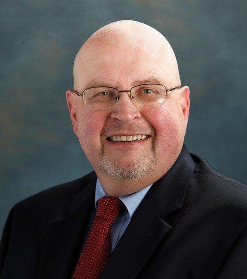 A bald man wearing glasses and a suit and tie smiles for the camera