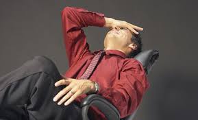 A man in a red shirt and tie is laying in an office chair.
