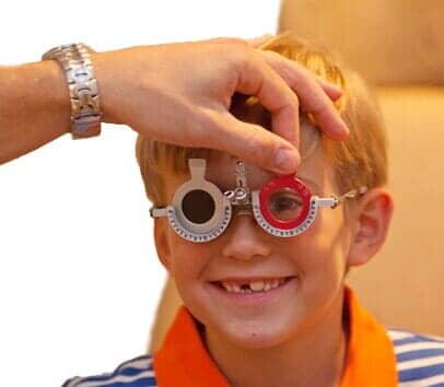 Child With Phoropter — Pediatric Eye Care in Charlottesville, VA A patient of a children's ophthalmology surgeon near Lynchburg, VA