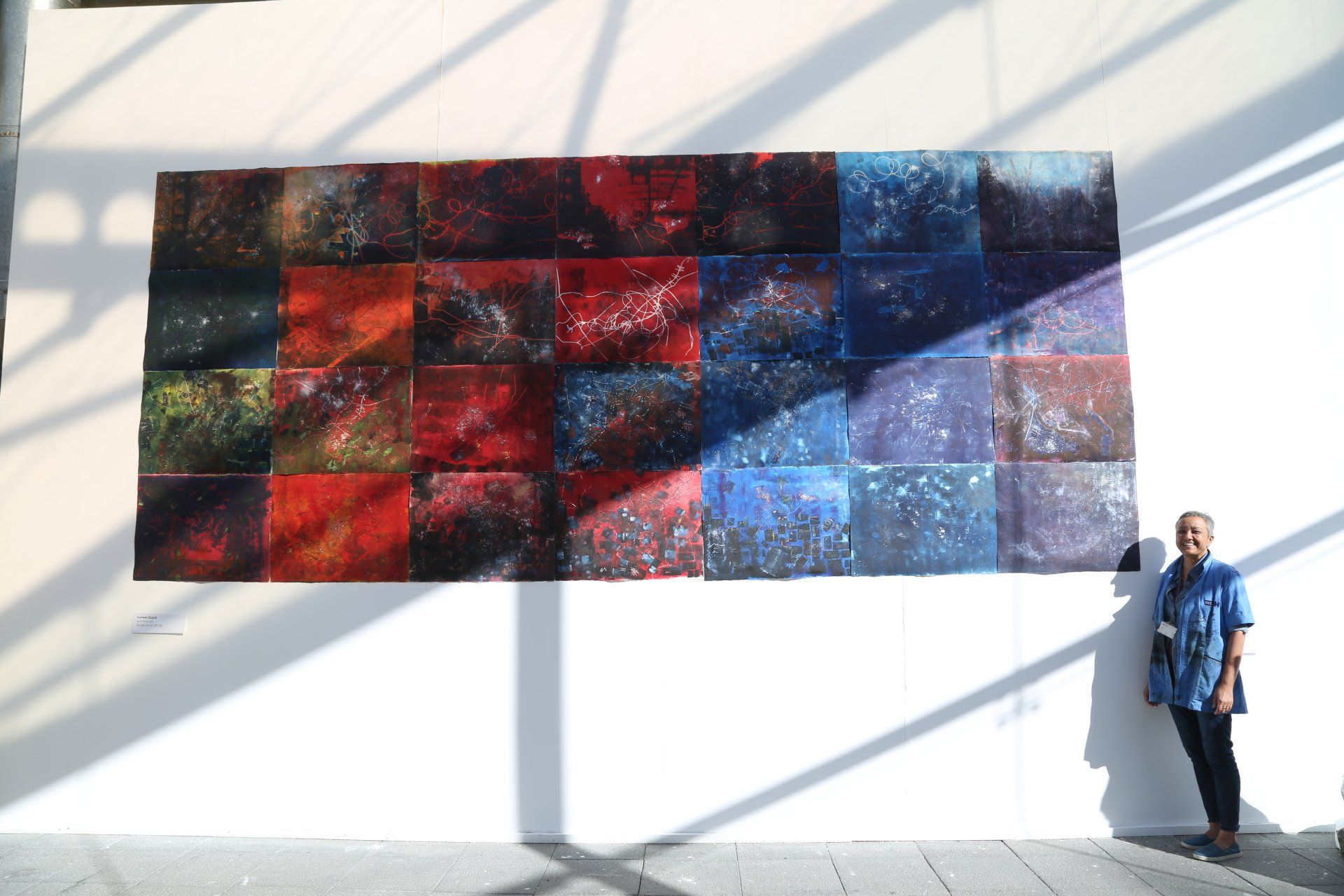 Large colorful square artwork with a person standing beside it. Reds, blues, and purples.