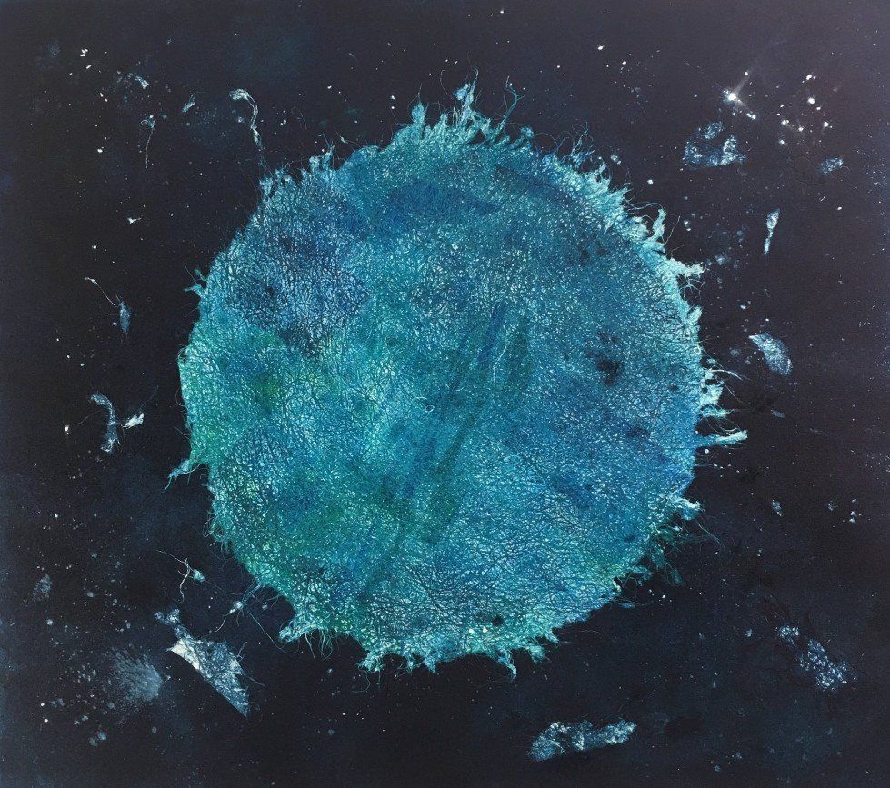 Blue, splattered circle on a black background, resembling a celestial body with scattered white specks.