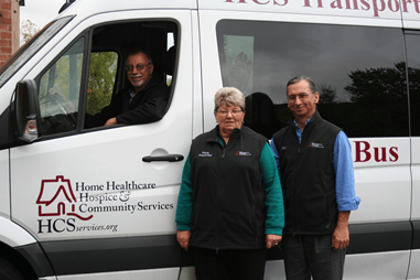 “Two staff members standing beside a Home Healthcare & Hospice Community Services transport van, with a driver visible inside.”