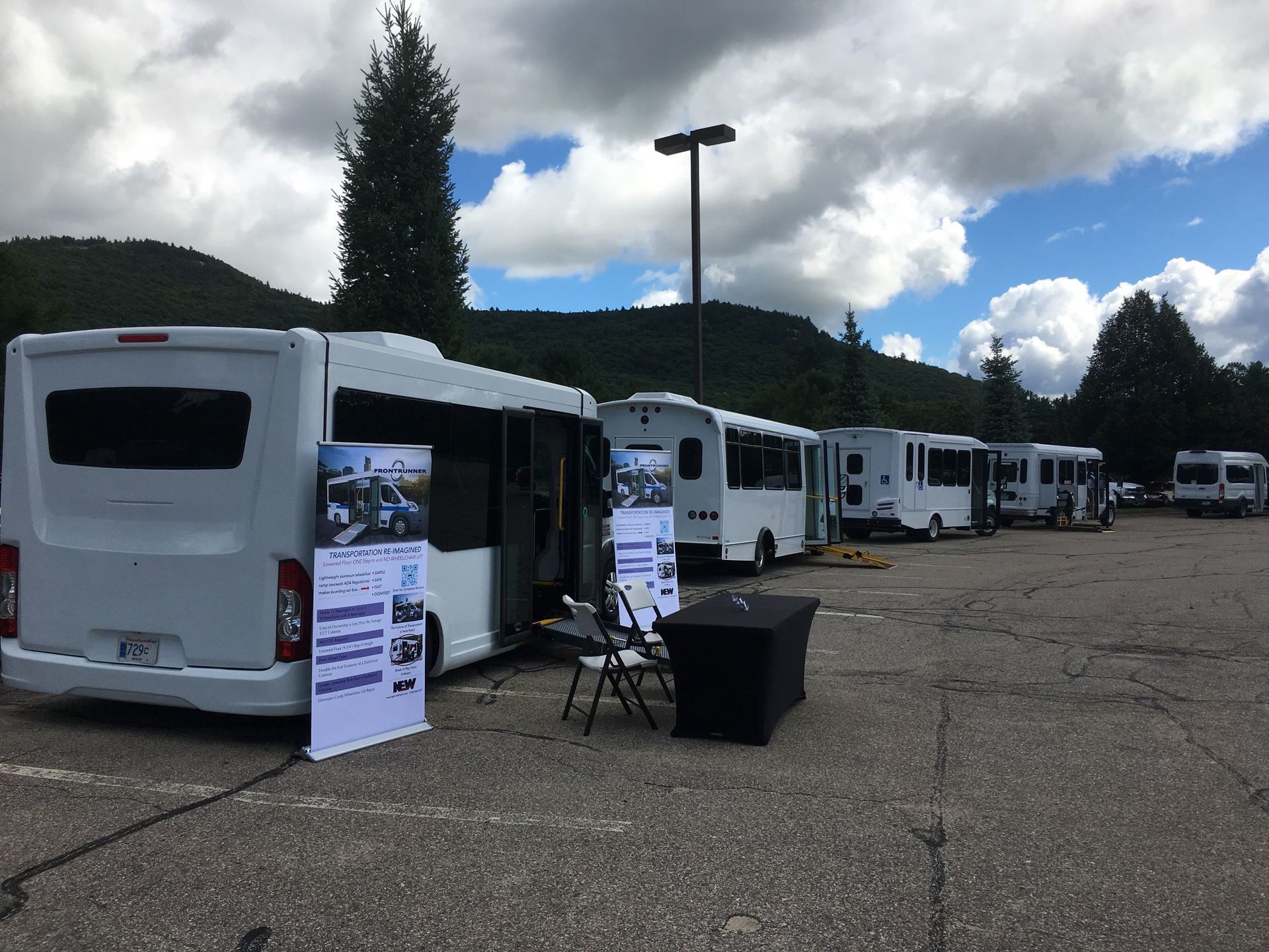 “Transit buses parked at an outdoor event with an information booth and display table set up nearby.”