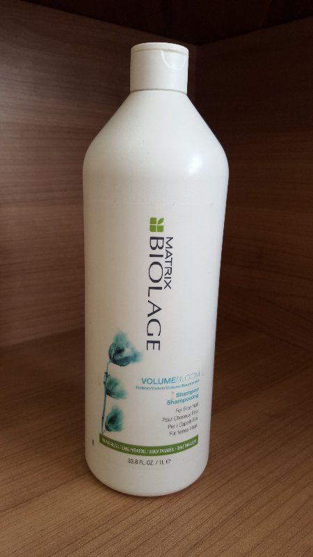 Weiße Flasche Matrix Biolage Shampoo mit grünen Akzenten auf einem Holzregal.