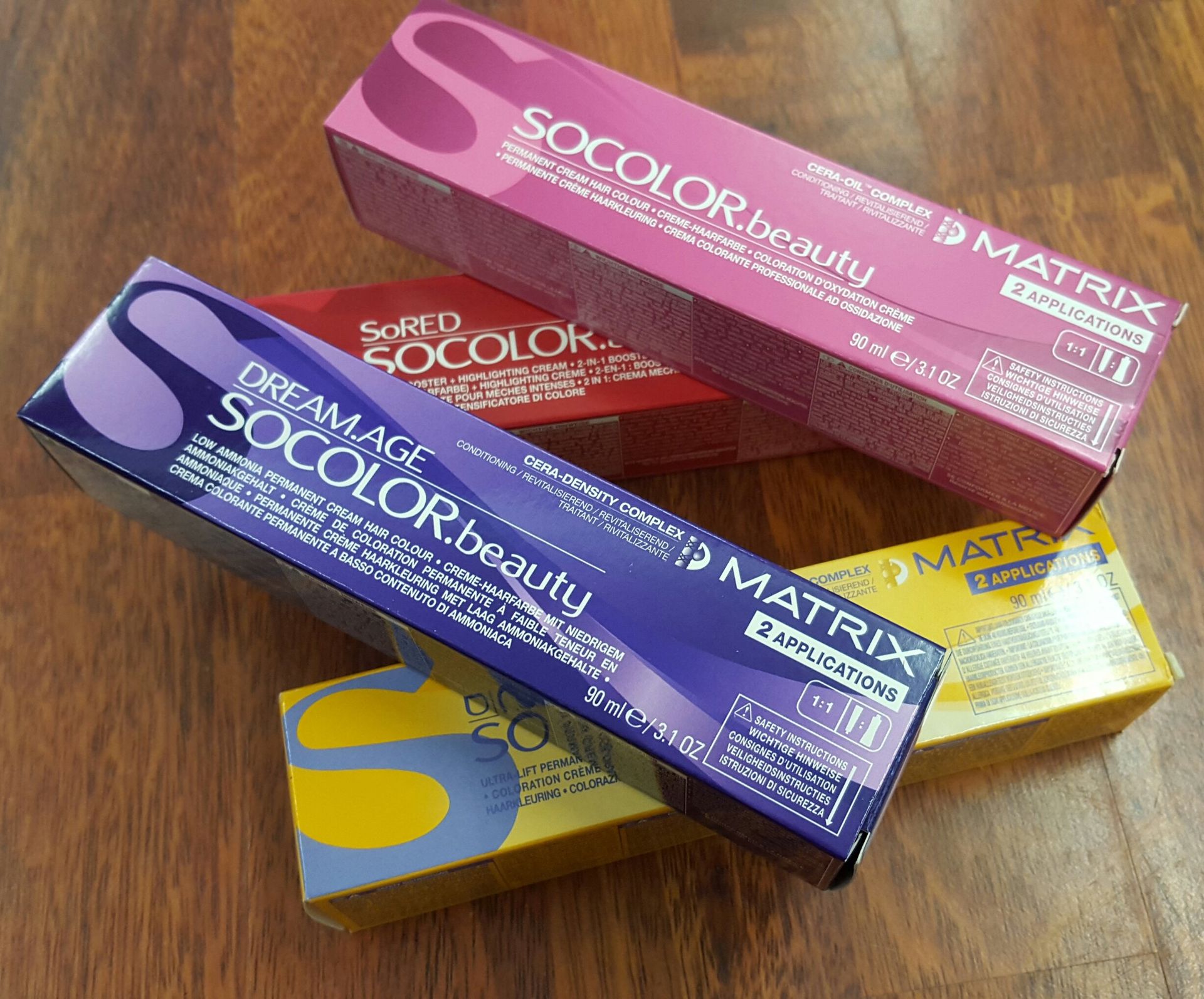 Vier Schachteln Matrix SoColor Beauty Haarfärbemittel in verschiedenen Farben sind auf einer Holzoberfläche gestapelt.