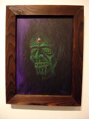 A painting of a green monster with a red eye is in a wooden frame on a wall.
