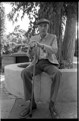 An elderly man is sitting on a bench with a cane.