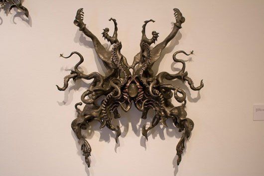 A sculpture of a spider is hanging on a white wall.