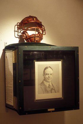 A baseball helmet is sitting on top of a display case next to a picture of a man.