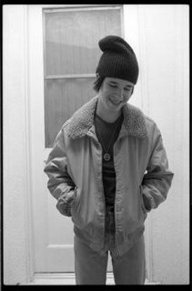 A young man wearing a beanie and a jacket is standing in front of a door.