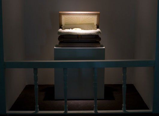 A coffin is on display in a dark room behind bars.