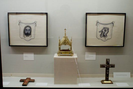 A display case with three crosses and two paintings on the wall.