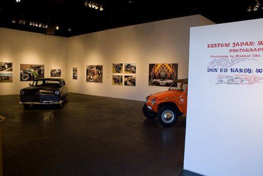 A car is parked next to a sign that says ' kustom japan ' on it