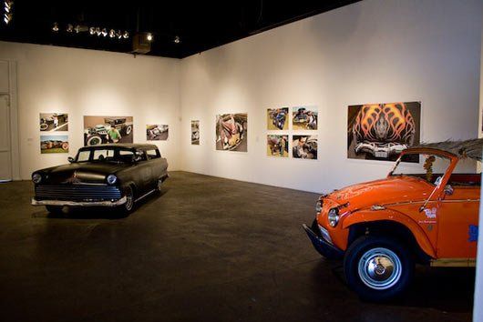 Two cars are parked in a room with pictures on the wall.