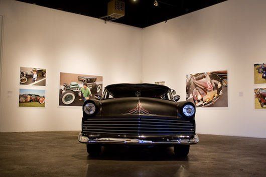 A black car is parked in a room with paintings on the wall.