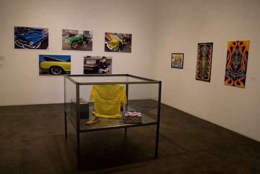 A glass case with a yellow shirt in it is in a room with pictures on the wall.